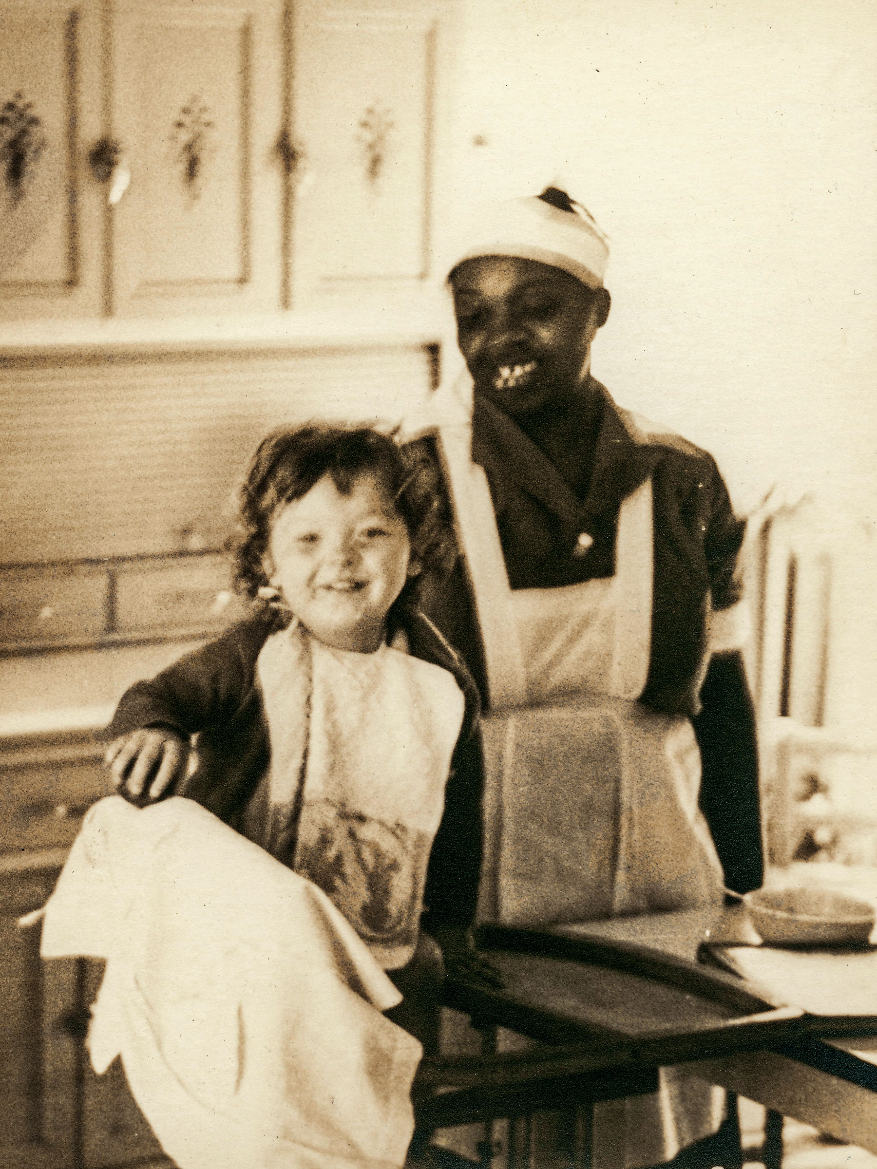 A vertical sepia portrait of Lucille Crowder, a Black domestic worker, and Bill Eggelston, a white child approximately age 3, posing for portrait.