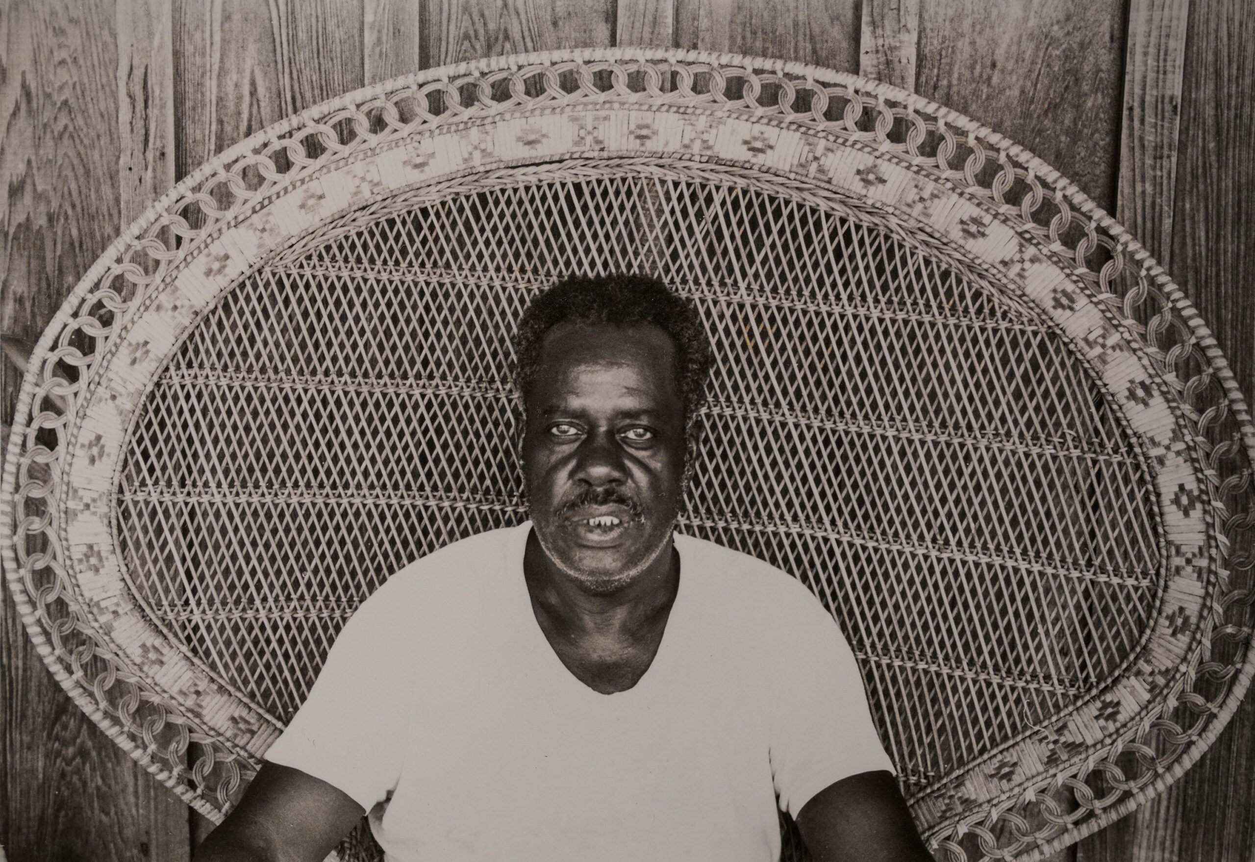 A black and white image of Jasper Staples seated in an ornate wicker chair.